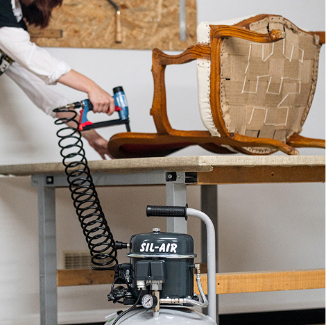 Artisan tapissier utilisant une agrafeuse pneumatique sur une chaise en cours de restauration, avec compresseur d'air